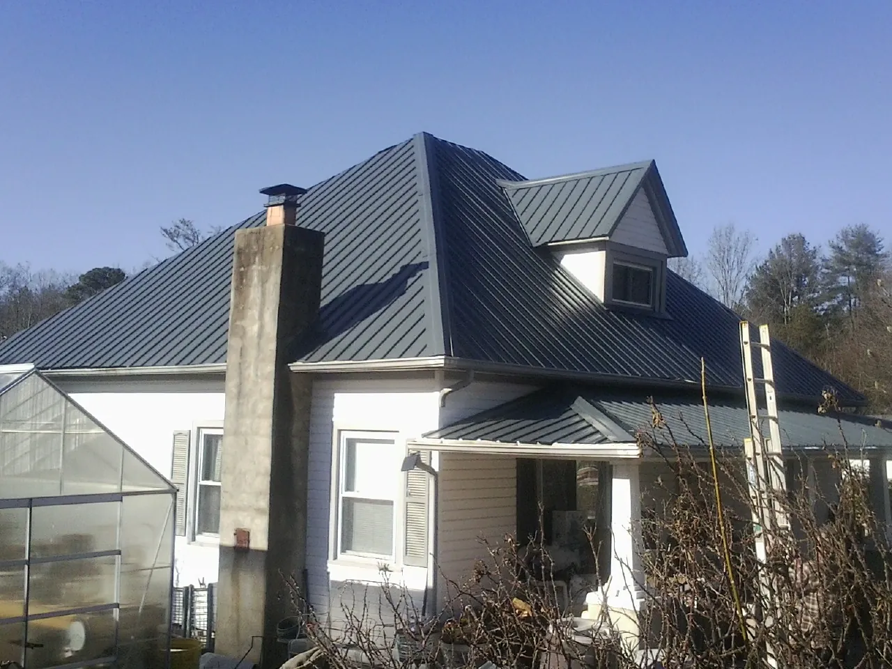 Dark blue standing seam metal roof on a white farmhouse with dormer — Slate & Tile Roof Repair by Roofing Brothers in Hampton Bays