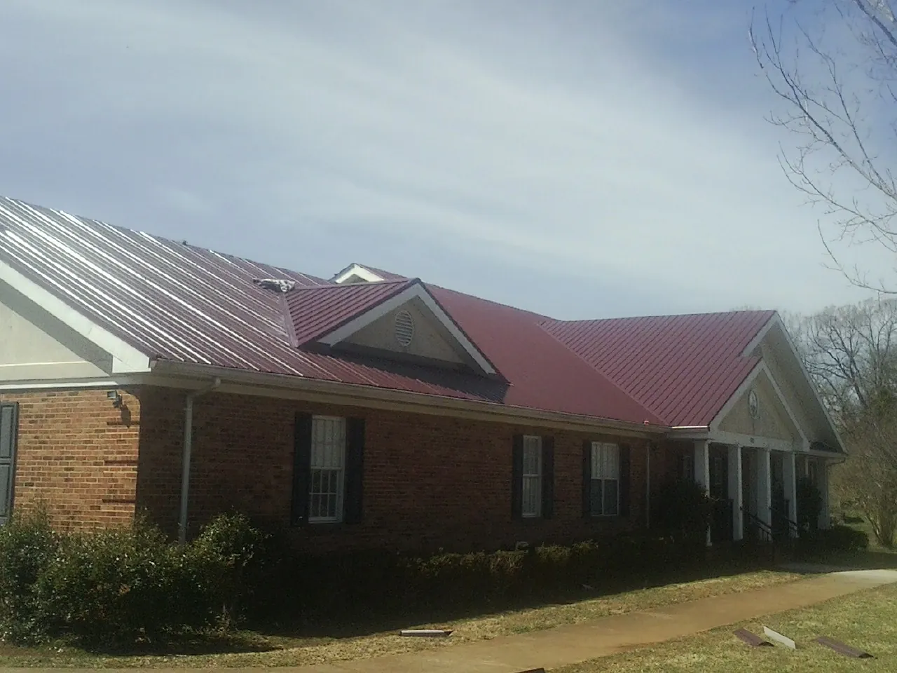 Red metal roof with gabled entries on a long brick building, from a Hail Damage Roof Repair job in Hampton Bays