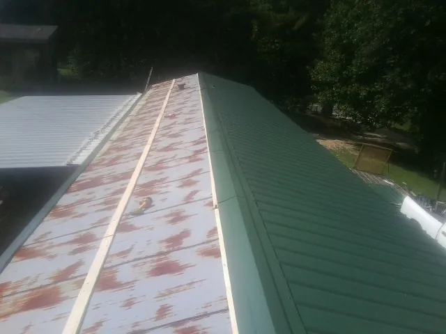 Old rusted panels beside newly installed green metal roofing — Wind Damage Roof Repair by Roofing Brothers in Hampton Bays