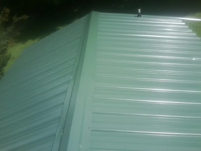 New green metal panels meeting at the ridge of a roof — Flat Roof Repair work by our crew in Hampton Bays