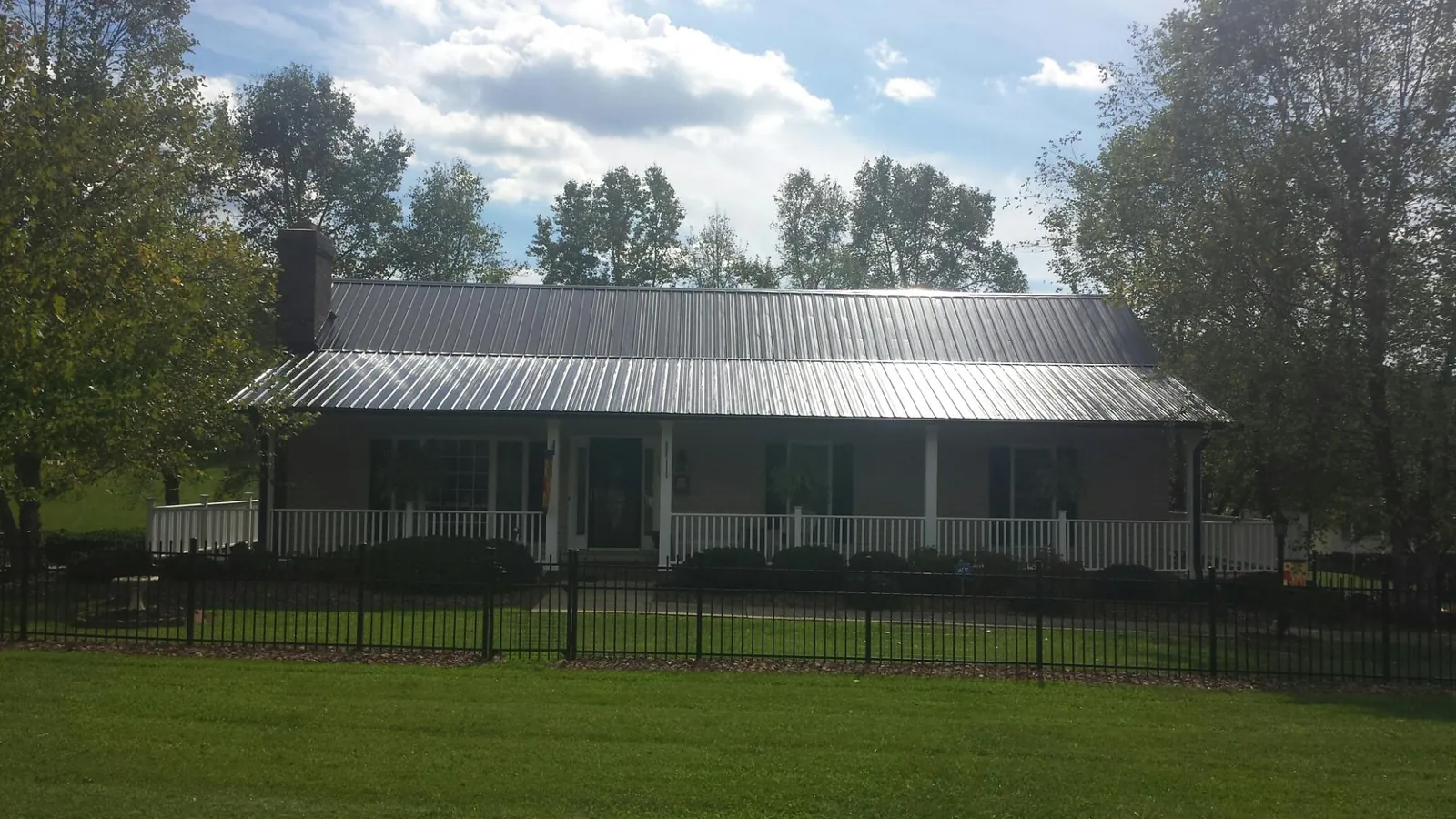 Gray metal roof on a brick ranch with a full width front porch — Gutter Guard Installation work by our crew in Hampton Bays