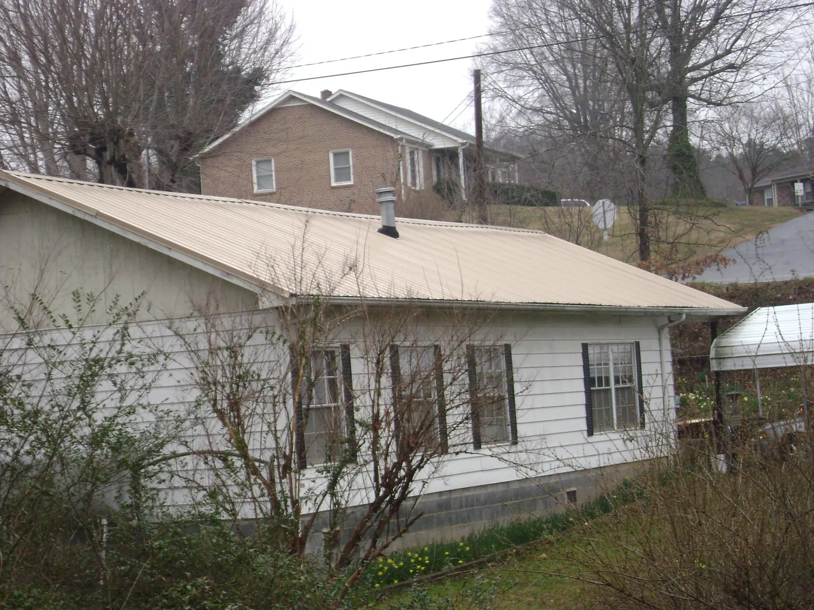 Tan metal roof on a white sided house set into a hillside — Commercial Roofing by Roofing Brothers in Hampton Bays